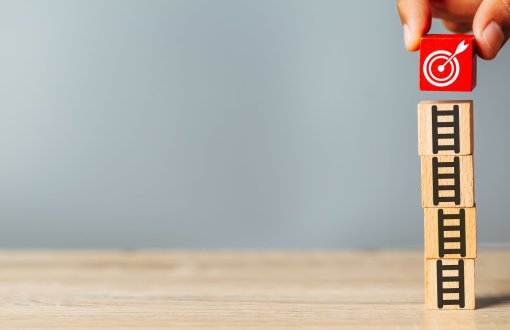 Kilka drewnianych klocków ustawionych jeden na drugim. Na szczycie klocek z wizerunkiem zegarka