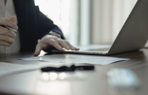 dłoń na biurku z kartką i laptopem